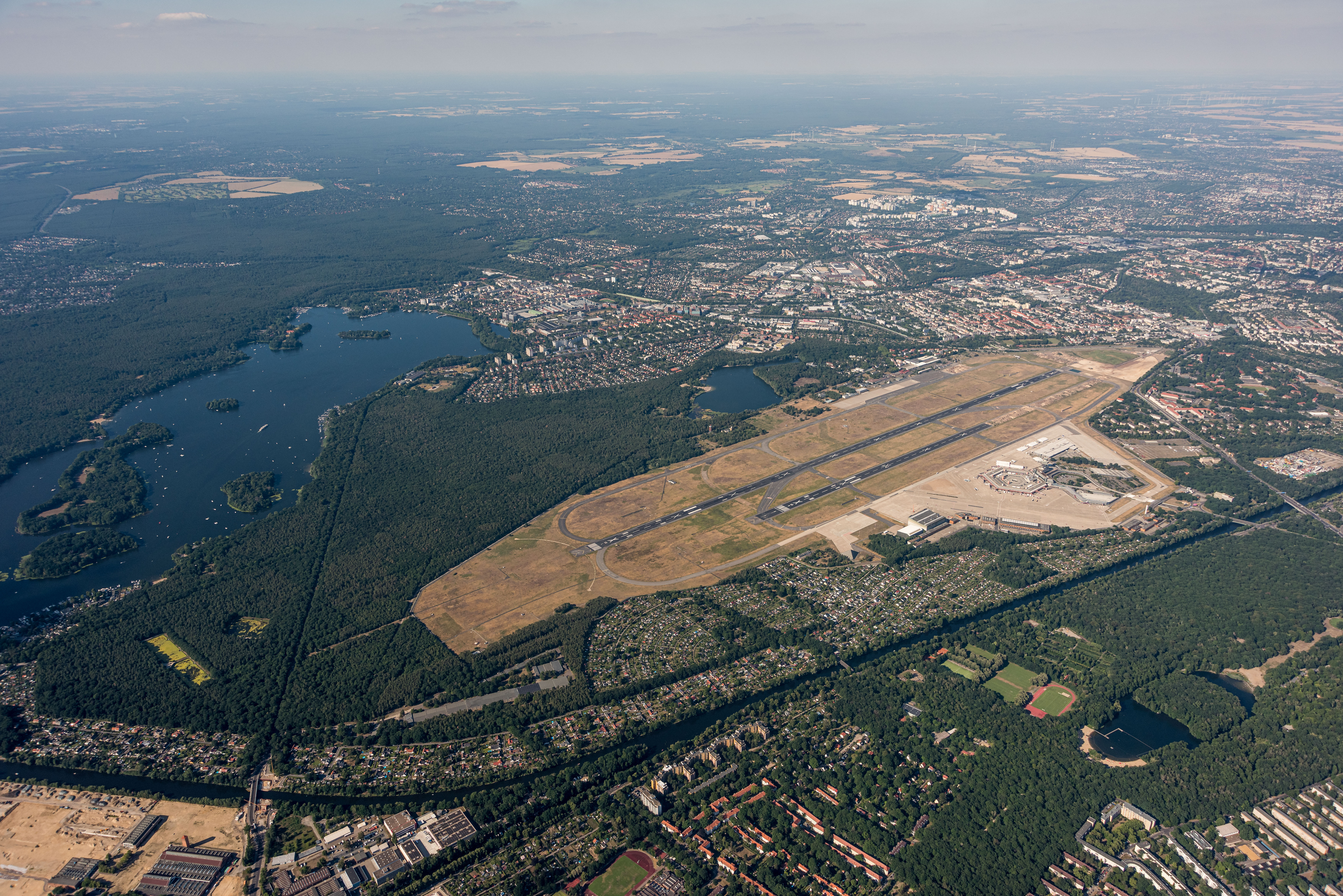 Aerial view of the former Berlin Tegel Airport with its runway, terminal buildings, surrounding forests, lakes and urban areas.