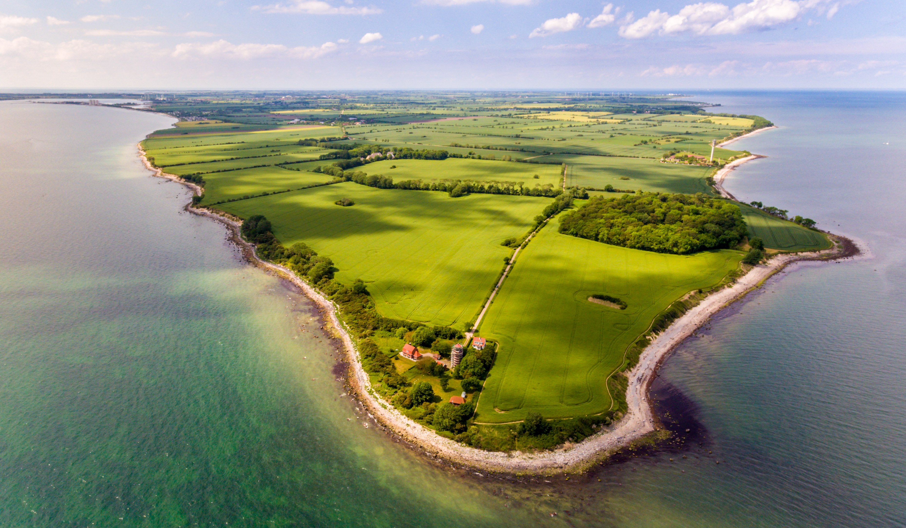 Aerial view of the island of Fehmarn with green fields, wooded areas and coastline along the Baltic Sea.