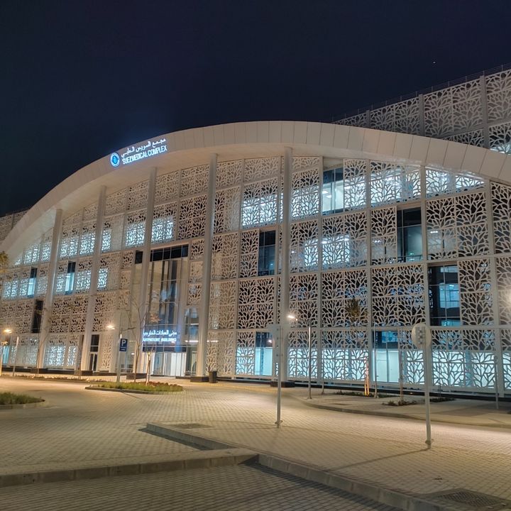 Illuminated outpatient building at the Suez Medical Complex, distinguished by a white façade with intricate organic-patterned screening panels.