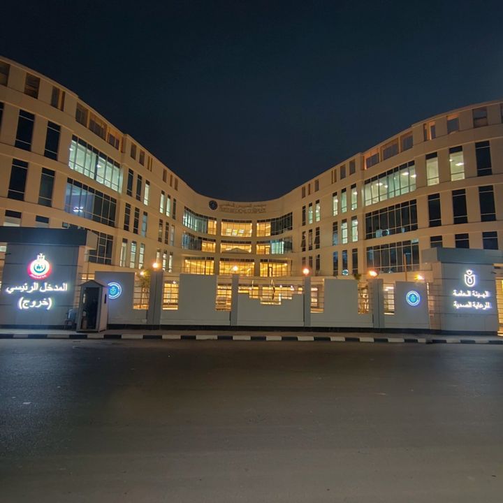 Night view of the illuminated main entrance of the Suez Medical Complex, framed by curved building wings and large windows.