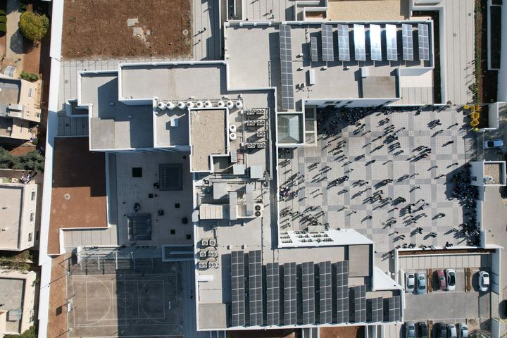 Bird view of a school building with solar panels on the roof and external recreational areas.