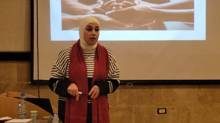 A women is standing with her back to a projected image, explaining something during the community engagement activities in Jdeitdet AlJoumeh.